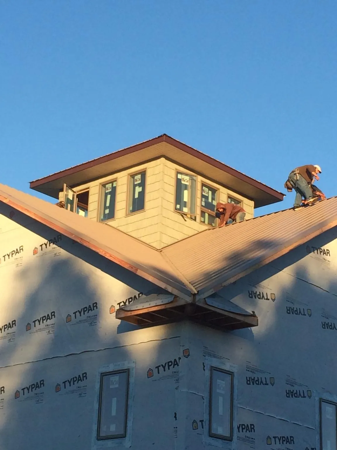 Roofers working around a rooftop cupola on a new metal roof at sunset — Roof Waterproofing in Highland by Roofing Brothers